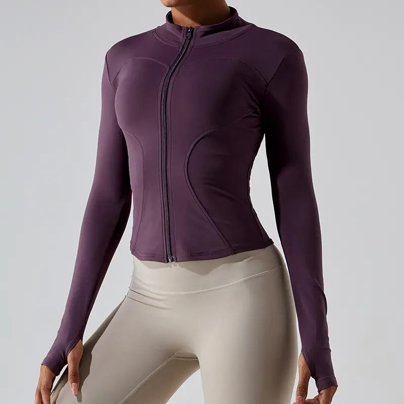 Woman wearing a fitted purple zip-up activewear jacket with thumbholes, paired with beige high-waisted leggings.
