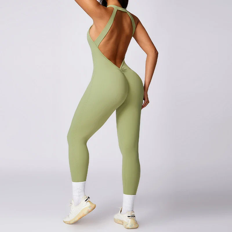 Woman wearing light green athletic jumpsuit with open back and scrunch detail, posing in studio.