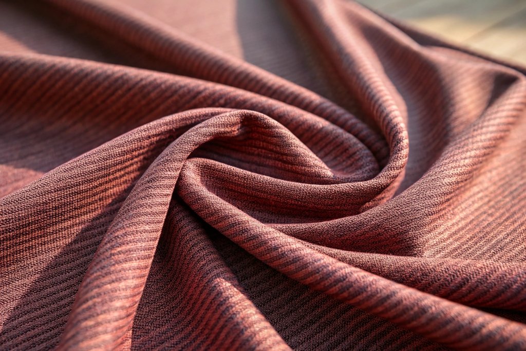Close-up of soft, ribbed reddish-brown knit fabric with natural folds and sunlight highlighting its texture.