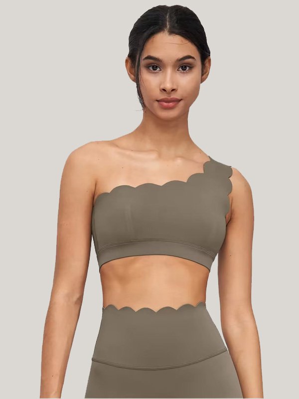 A woman wearing a tan one-shoulder sports top with scalloped edges, paired with matching leggings, showcasing a unique and stylish design.