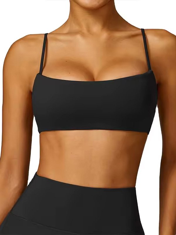 A woman wearing a black spaghetti strap sports bra, featuring a simple, sleek design with a straight cut.