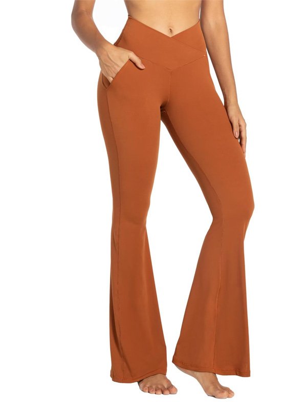 A pair of high-waisted flare yoga pants in rust, featuring a flattering V-shaped waistband and side pockets, worn by a model barefoot, emphasizing comfort and style