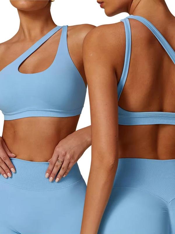 A close-up shot of a woman wearing a blue one-shoulder sports bra, showcasing its sleek design with a cut-out detail, paired with high-waisted matching leggings
