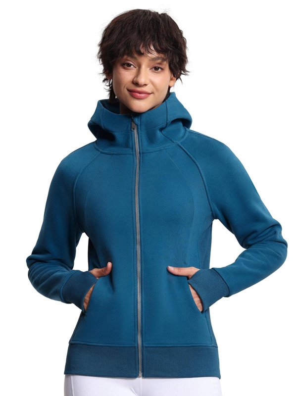 A woman wearing a teal zip-up hoodie with a high collar, featuring side pockets, paired with white leggings, creating a cozy and casual athleisure look.