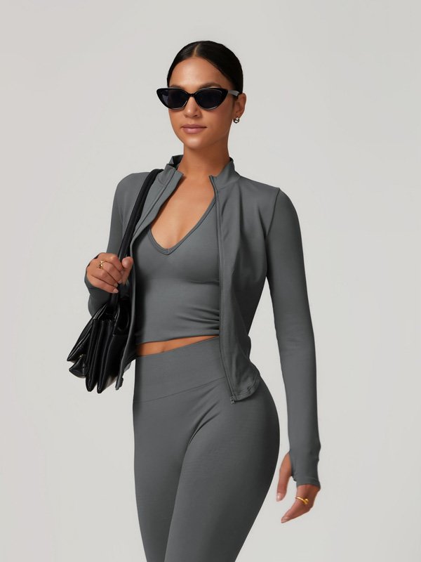 A woman wearing a grey zip-up jacket, matching sports bra, and leggings, accessorized with sunglasses and a black handbag, showcasing a sleek and modern athleisure look