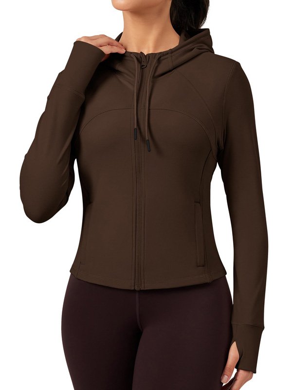 A woman wearing a brown zip-up hoodie with a hood, featuring side pockets and long sleeves, paired with dark leggings, showcasing a stylish and functional athleisure look