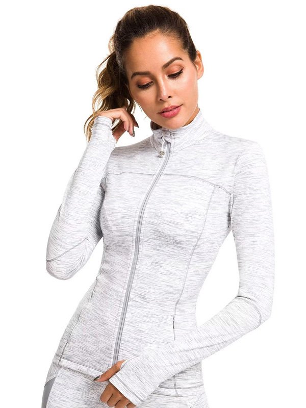 A woman wearing a light grey zip-up athletic jacket with a high collar and long sleeves, featuring thumb holes, showcasing a chic and functional activewear look