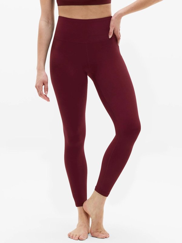 A front view of a woman wearing high-waisted maroon leggings, styled with a matching sports bra. The leggings feature a sleek, full-length fit ideal for active or casual wear
