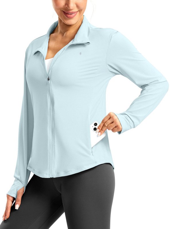 A woman wearing a light blue zip-up athletic jacket with a phone in the pocket, paired with black leggings, showcasing a functional and stylish activewear look