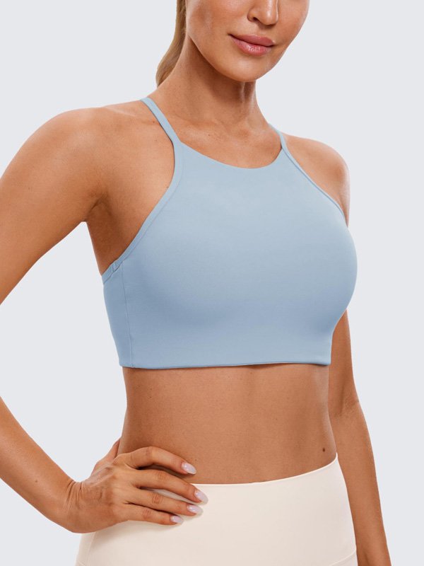 A woman wearing a light blue halter neck sports bra, showcasing a smooth, minimal design with a comfortable fit.