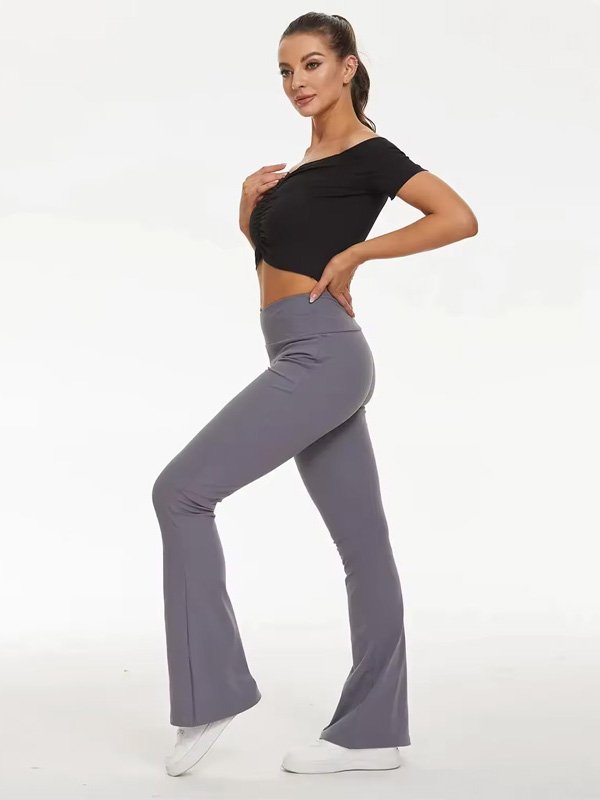 A side view of a woman wearing high-waisted grey flared leggings paired with a black crop top and white sneakers. The leggings feature a snug fit through the thighs and a flare at the hem.