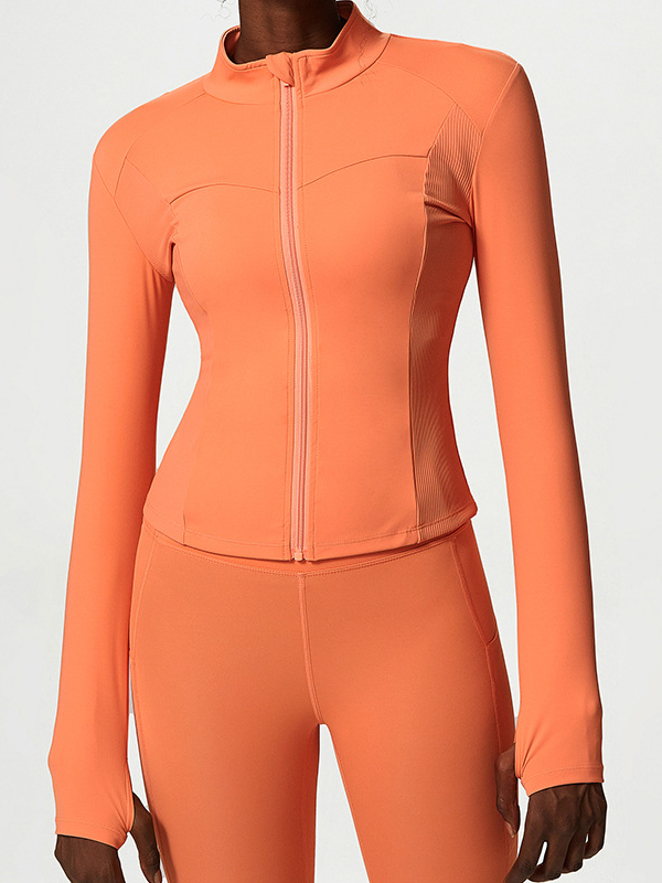 A woman wearing a zip-up orange athletic jacket, featuring a high collar and ribbed detailing, paired with matching leggings, showcasing a modern and sporty athleisure style