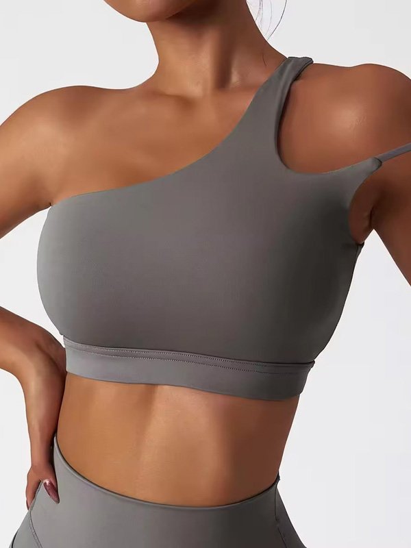 A woman wearing a grey one-shoulder sports bra, paired with matching leggings, showcasing a minimalist and modern design.