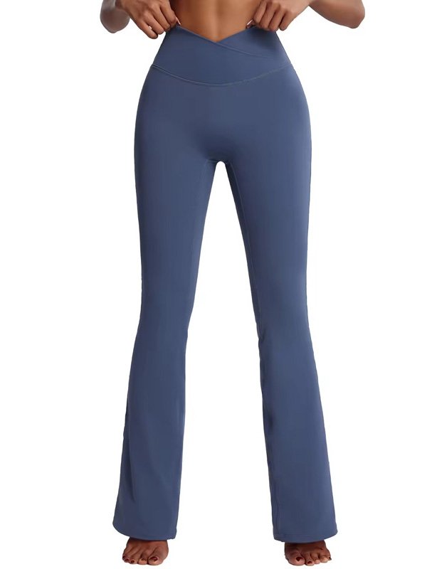 A front view of a woman wearing high-waisted blue flared leggings with a crossover waistband. The leggings have a fitted silhouette through the thighs and flare out at the bottom, styled barefoot.