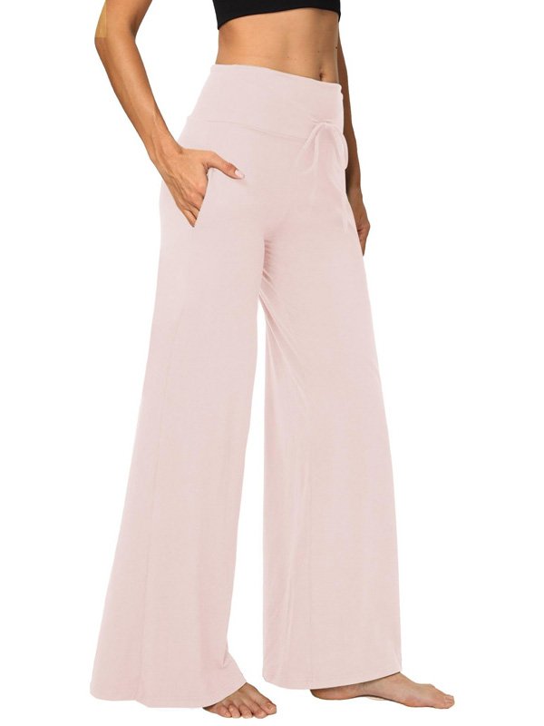 A pair of wide-leg custom yoga pants in soft pink with a drawstring waistband and side pockets, worn by a model barefoot, showcasing comfort and style