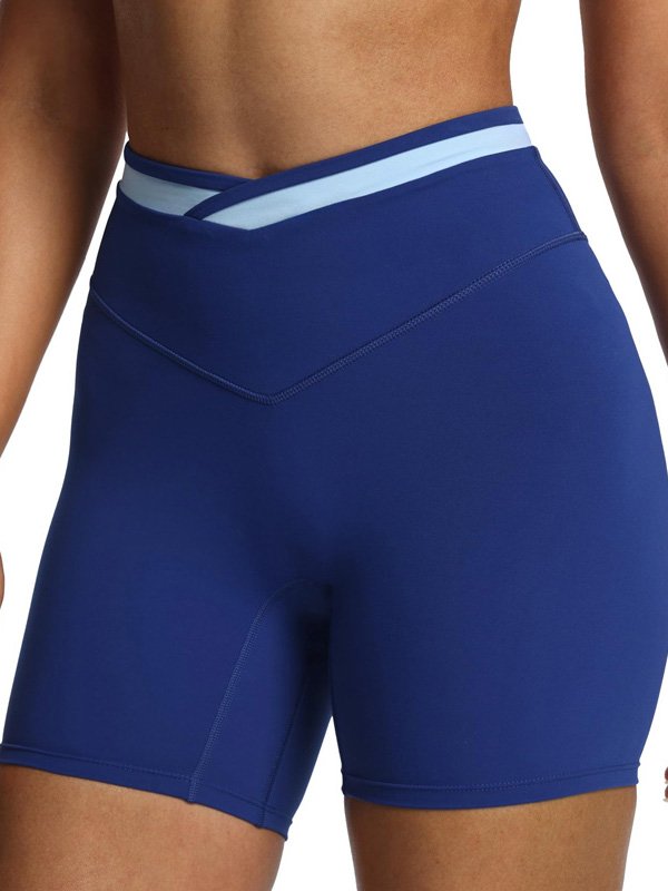 Woman wearing high-waisted blue athletic shorts with a light blue waistband design, highlighting a smooth, stretchy fit and stylish cross-waist detail.