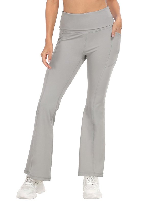 A pair of high-waisted, flared yoga pants in light gray, featuring side pockets, worn by a model in white sneakers, showcasing comfort and a flattering fit