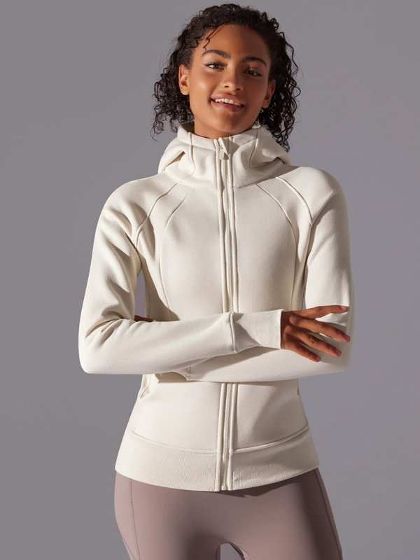 A woman wearing a white zip-up hoodie with a high collar and long sleeves, paired with light brown leggings, showcasing a sporty and comfortable look.