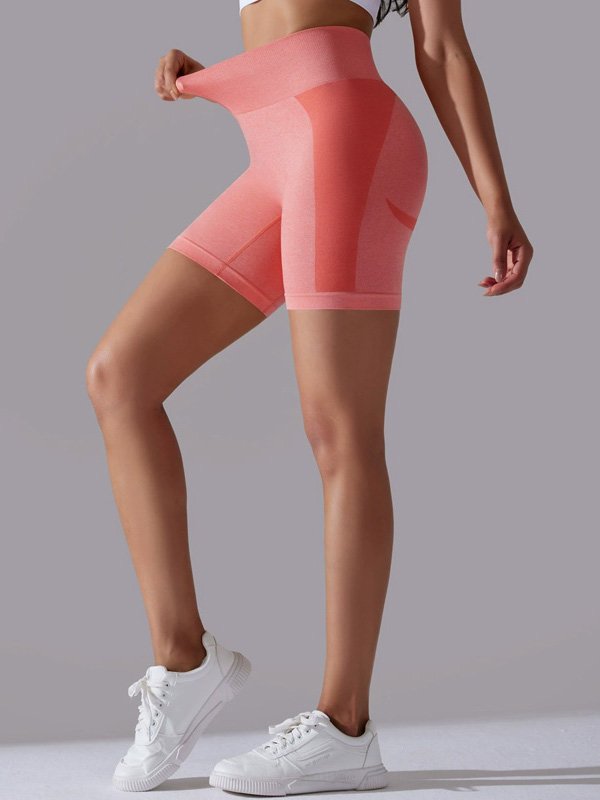 Woman wearing high-waisted coral athletic shorts, adjusting the waistband, paired with white sneakers, showcasing a smooth, fitted design.
